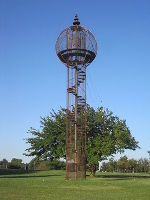 a tall metal tower sitting in the middle of a field next to a tree and blue sky