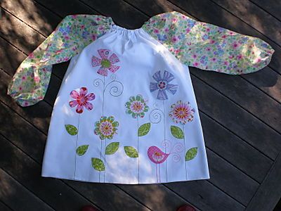 a child's dress with flowers and leaves on it, sitting on a wooden deck