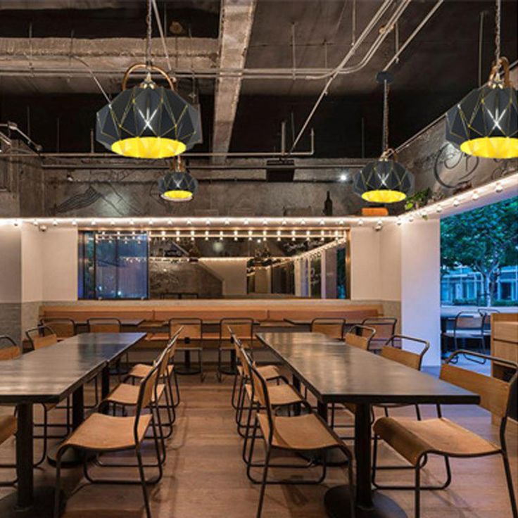 an empty dining room with wooden tables and chairs, yellow lights hanging from the ceiling