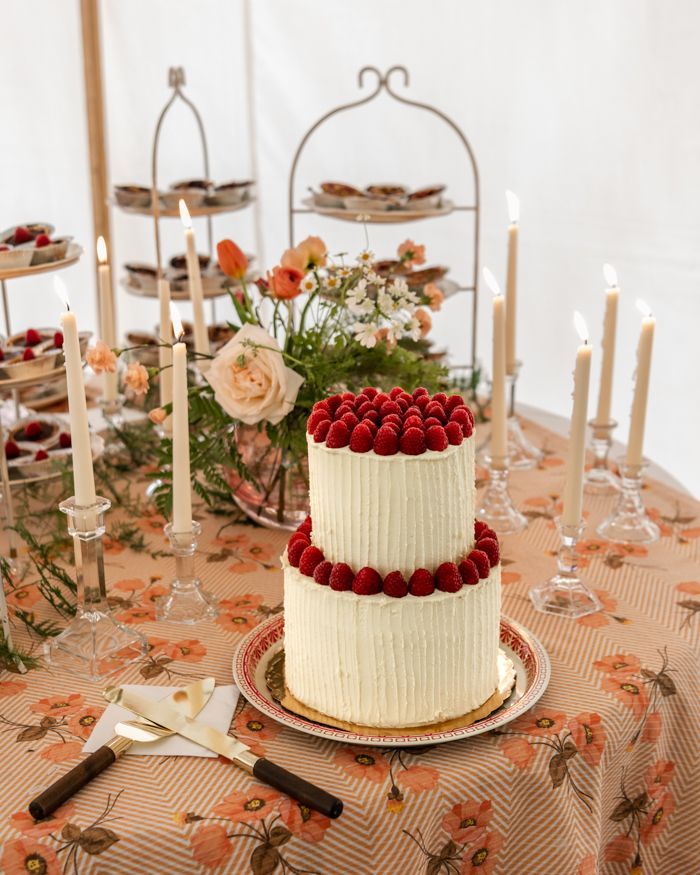 a white cake with raspberries on it sitting on top of a table next to candles