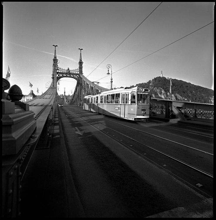 two trains passing each other on tracks in front of a bridge and mountains with power lines above them