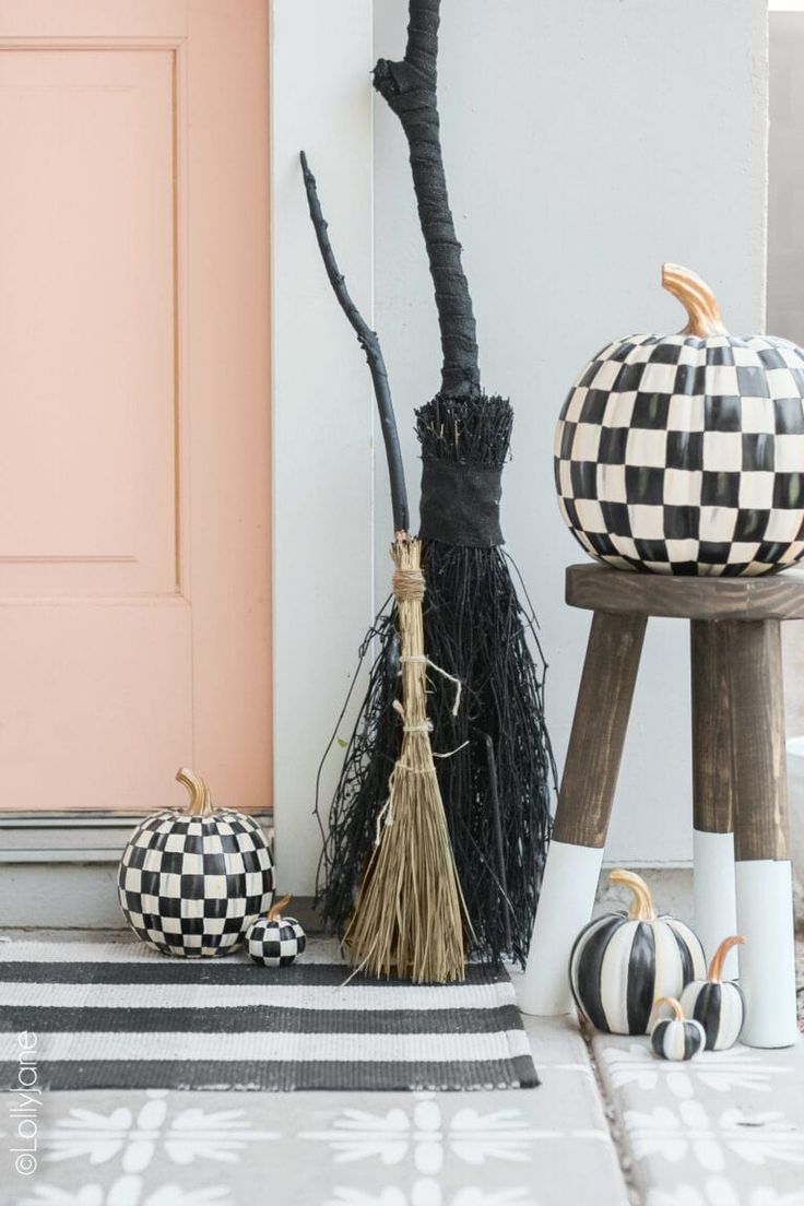 two black and white pumpkins sitting on top of a wooden stool next to a pink door