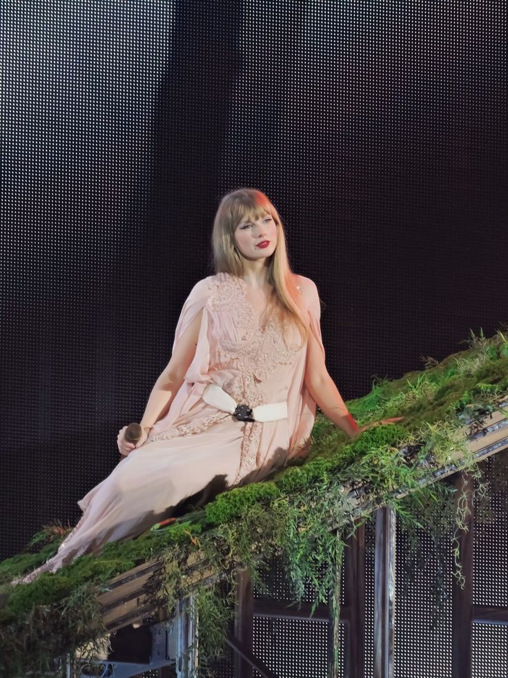 a woman sitting on top of a fence covered in green plants and mossy grass