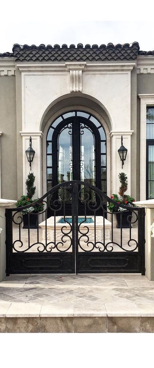 a black iron gate with potted plants on the top and below it in front of a house