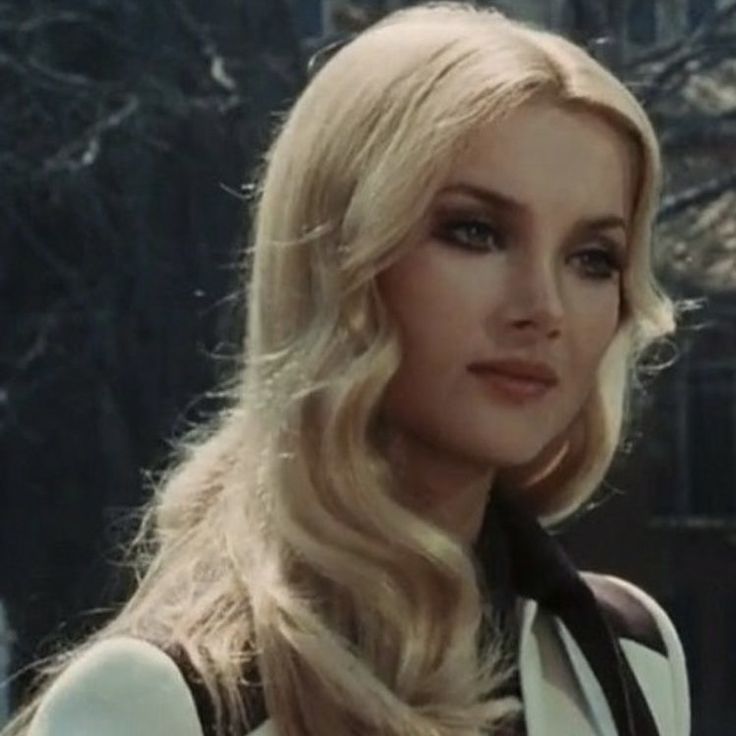 a woman with long blonde hair wearing a white jacket and black bow tie standing in front of a building