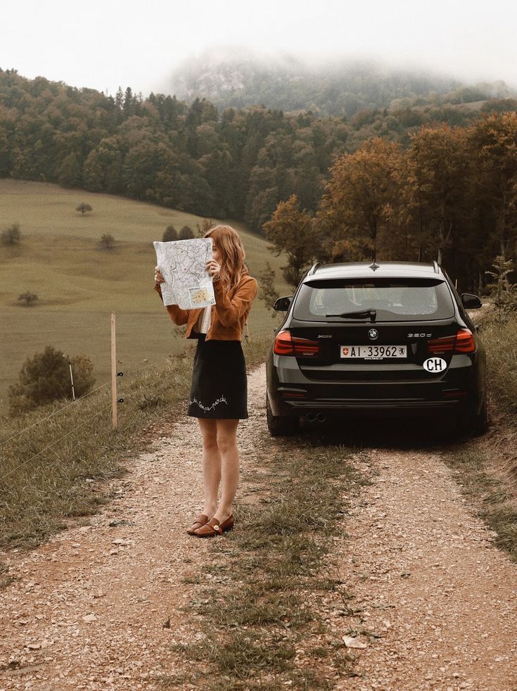 a woman standing on a dirt road next to a car holding up a piece of paper