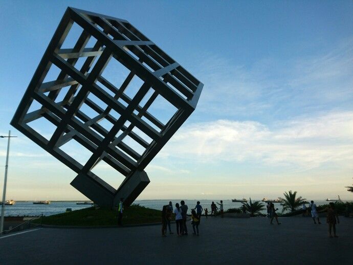 several people are standing in front of a large metal object near the water's edge