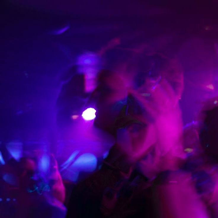 a group of people standing around each other in front of purple and blue lights at a party