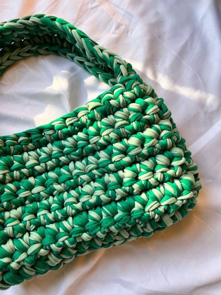 a green and white woven purse laying on top of a bed next to a pillow