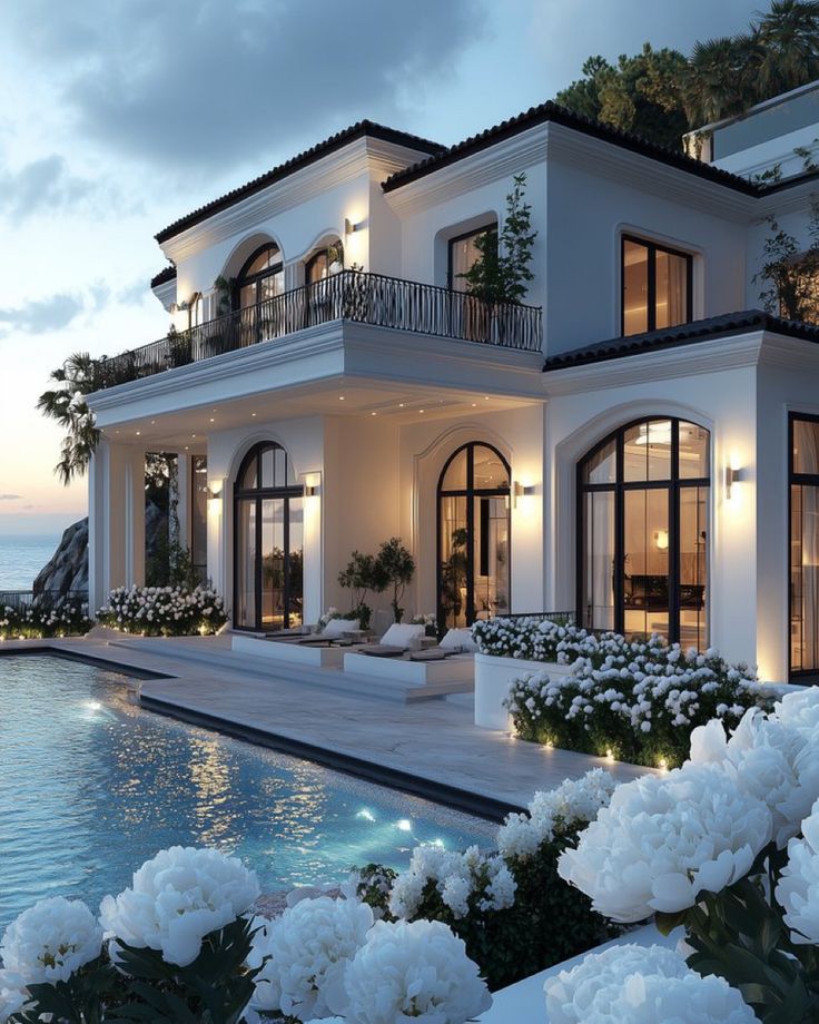 a large white house next to a swimming pool at dusk with flowers in the foreground