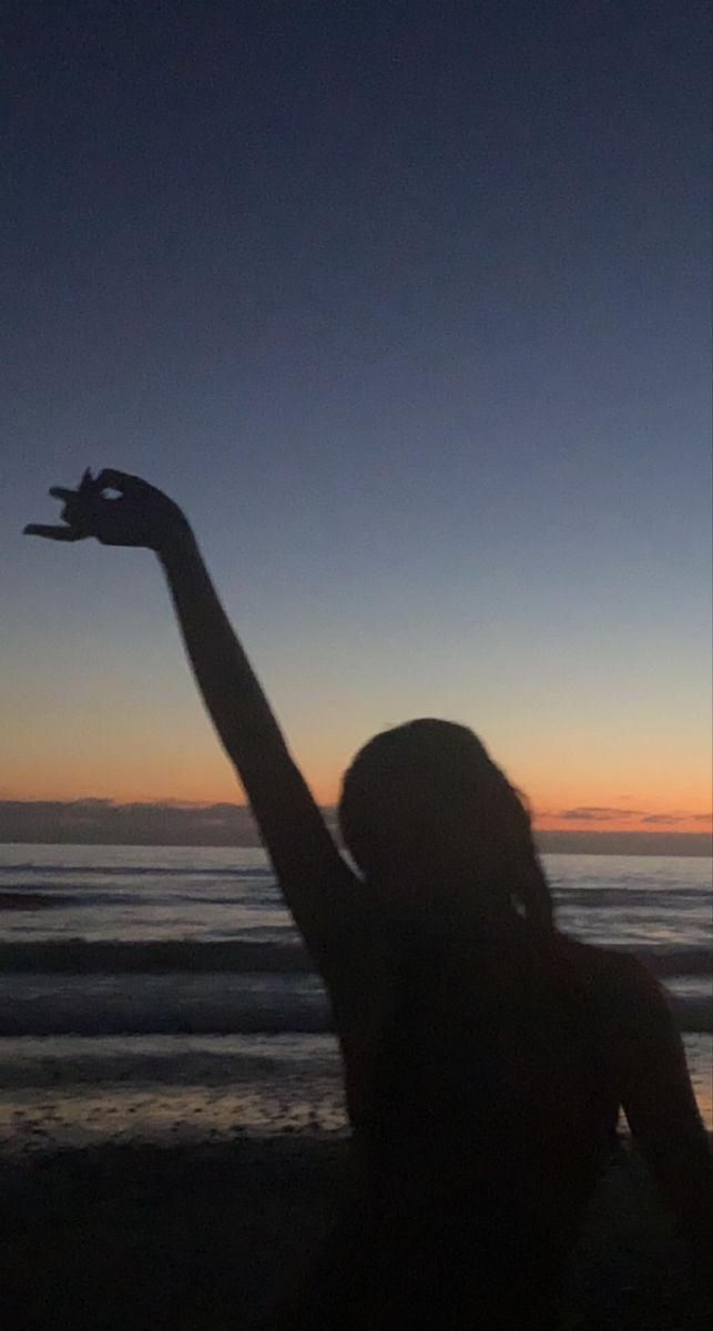 a woman sitting on the beach holding her arm in the air