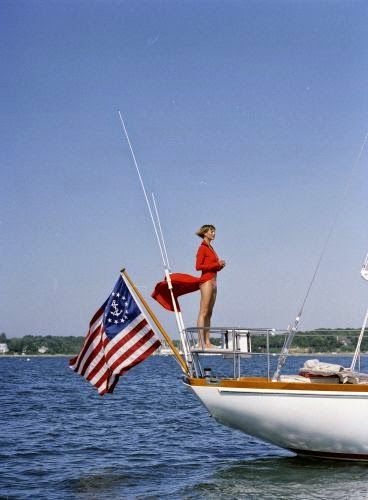 a woman standing on the bow of a sailboat with an american flag flying from it