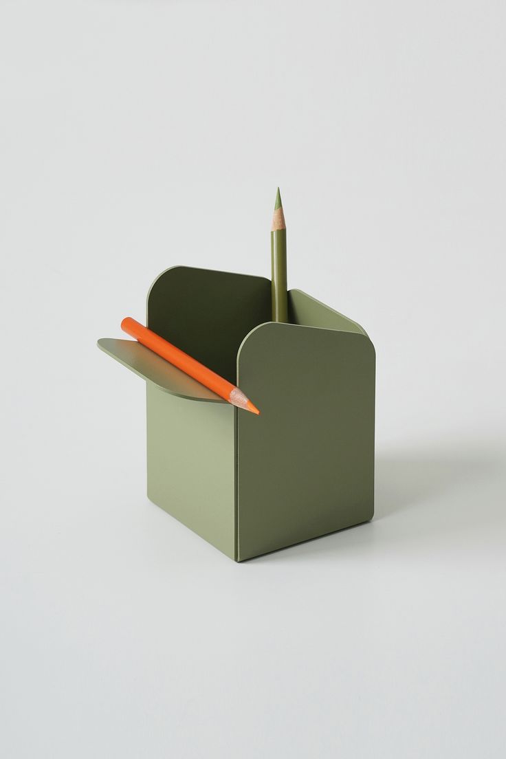 a pen holder with two pencils in it on a white surface, next to a green box