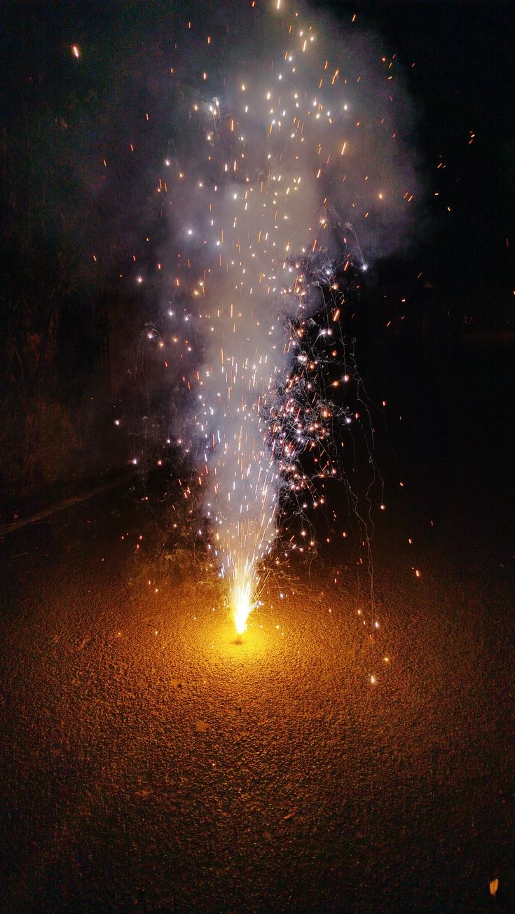 fireworks are lit up in the night sky over a street with trees on both sides