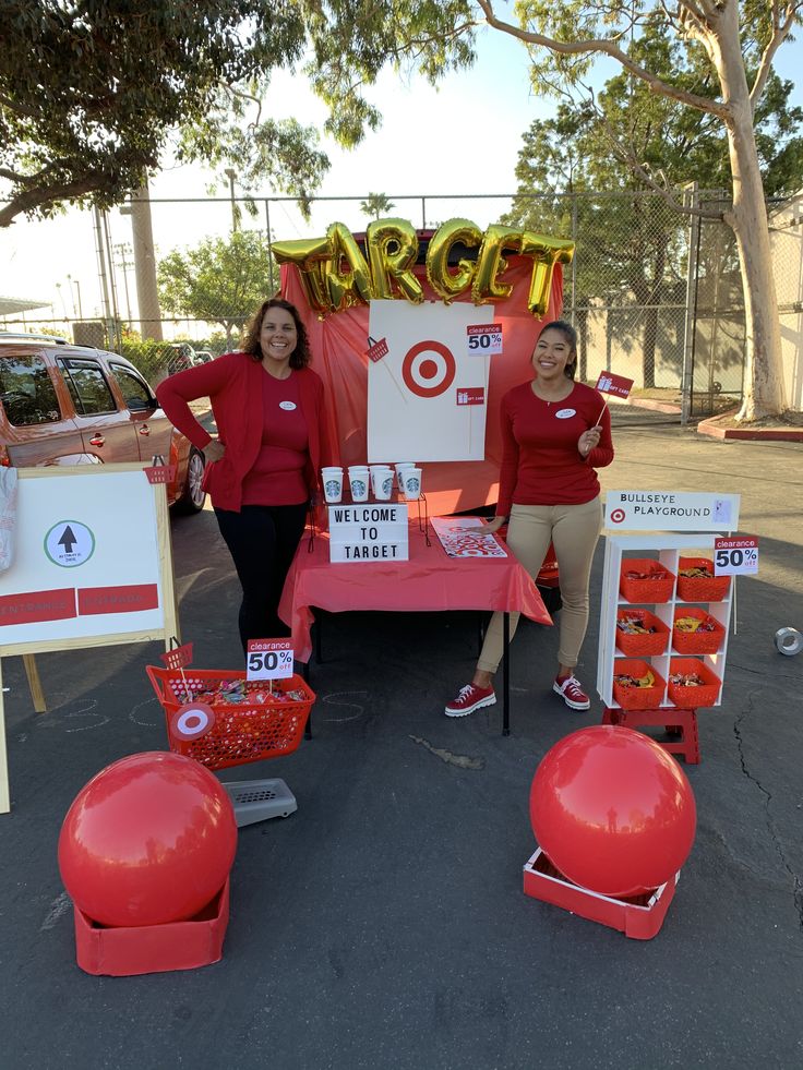 two women in red shirts are standing behind a table with balloons and signs on it