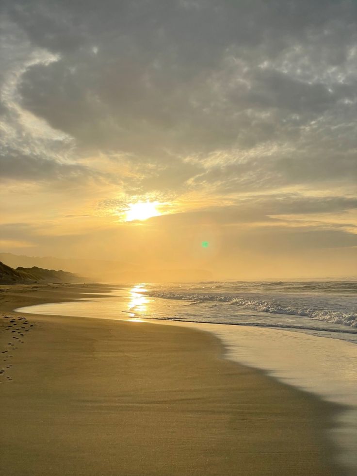 the sun is setting over the beach with footprints in the sand and water on the shore