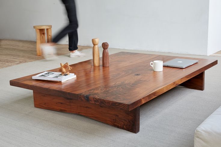 a person walking past a coffee table in a living room with white carpet and wooden furniture