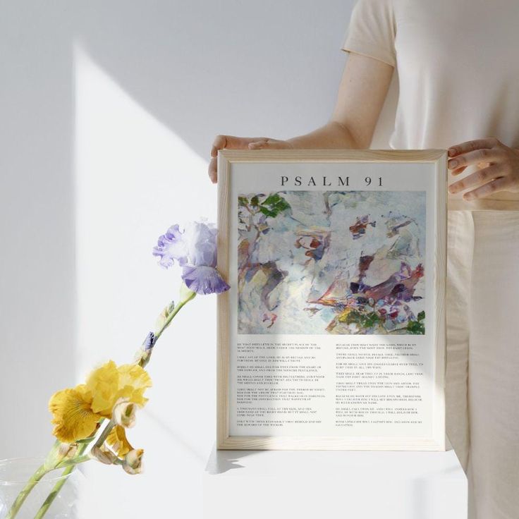 a woman holding up a framed poster with flowers in front of her