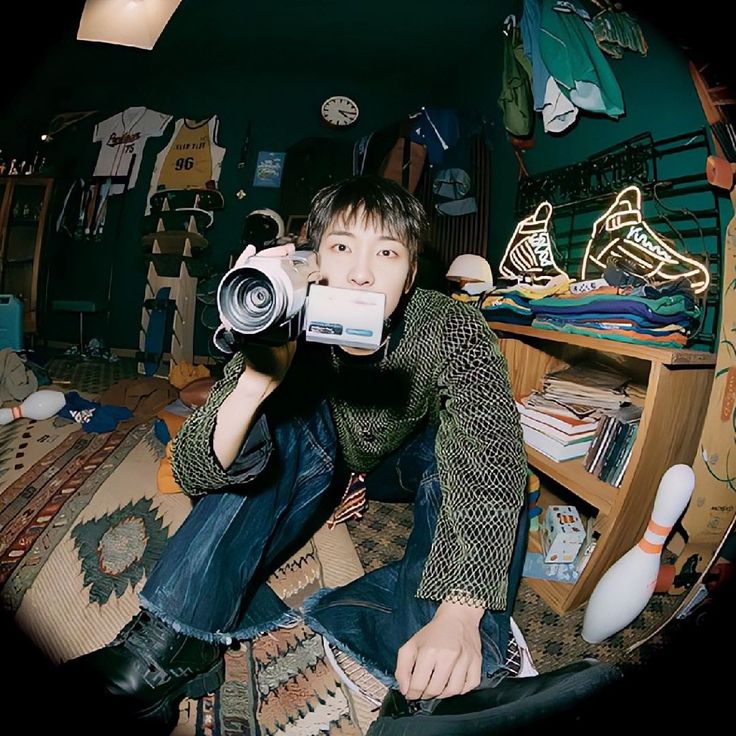 a young man sitting on the floor with a camera in his hand, taking a selfie