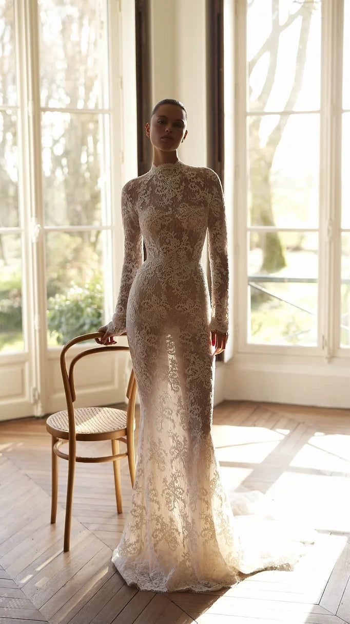 a woman in a long sleeved wedding dress standing on a wooden floor next to a chair