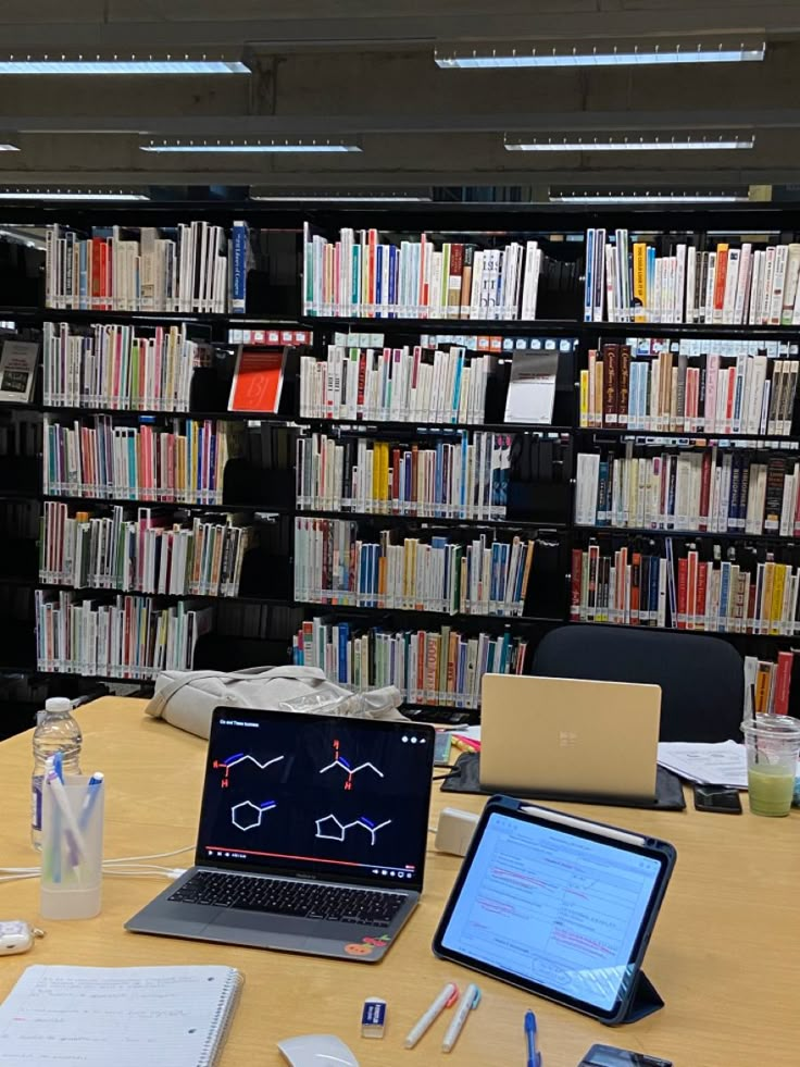 two laptops are sitting on a table in front of a bookshelf full of books