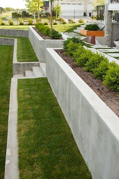 an outdoor garden with grass and plants in the center, surrounded by concrete blocks on either side