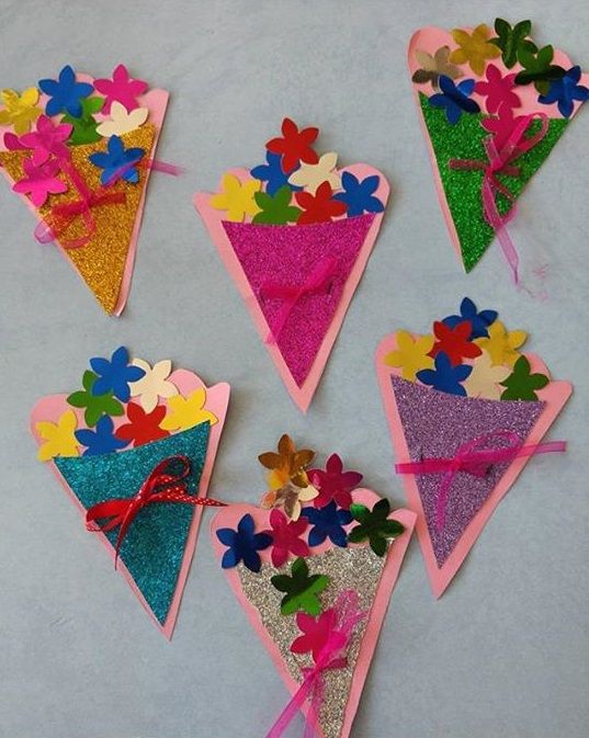 paper flowers are attached to colorful kites on a gray surface with pink, blue, yellow and green colors