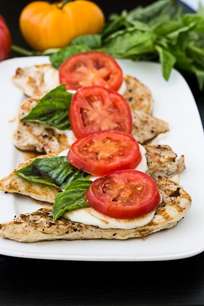 a white plate topped with chicken, tomatoes and spinach on top of a table