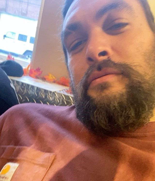 a man with a goatee and beard sitting in front of a table holding a cell phone