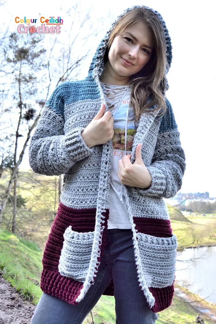 a young woman wearing a crocheted hooded jacket and giving the thumbs up sign