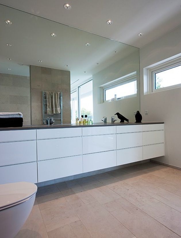 a bathroom with a toilet, sink and large mirror in the wall next to it