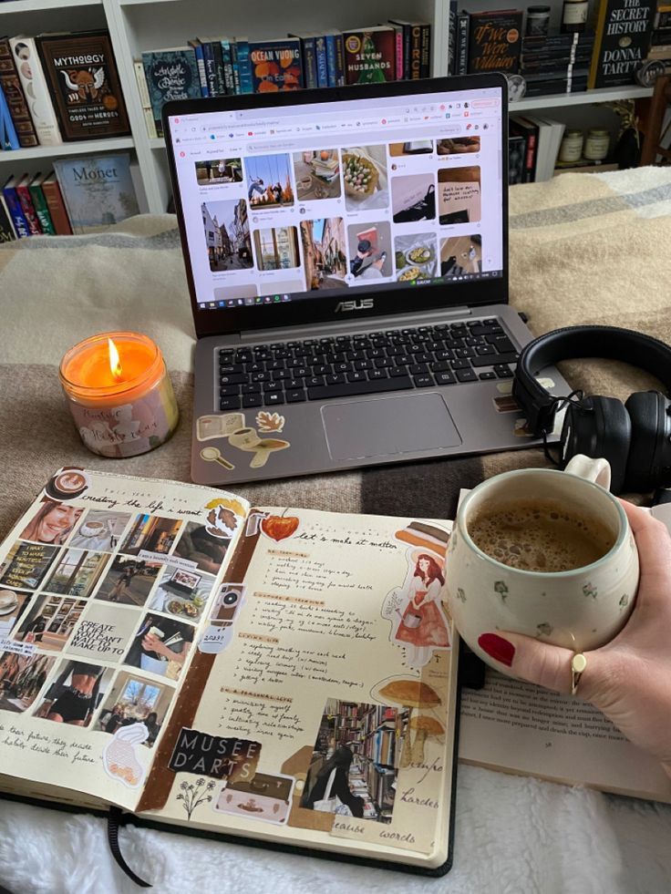 a person holding a cup of coffee in front of a book and laptop on a bed