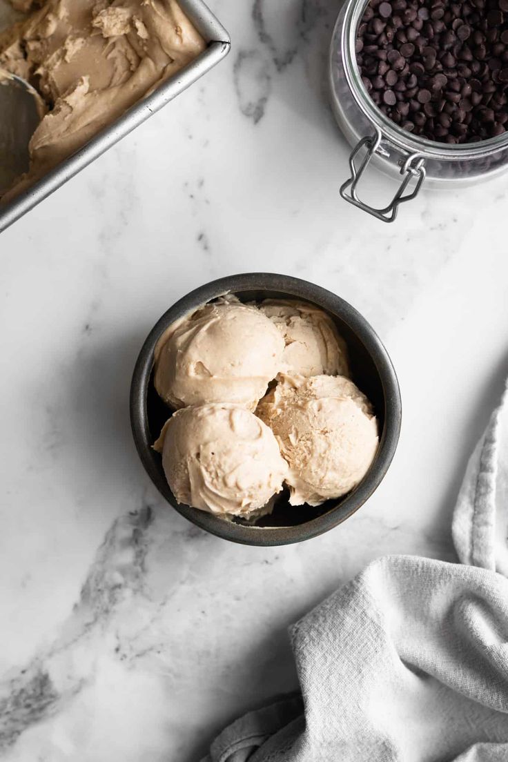 three scoops of ice cream in a bowl on a marble counter top next to chocolate chips