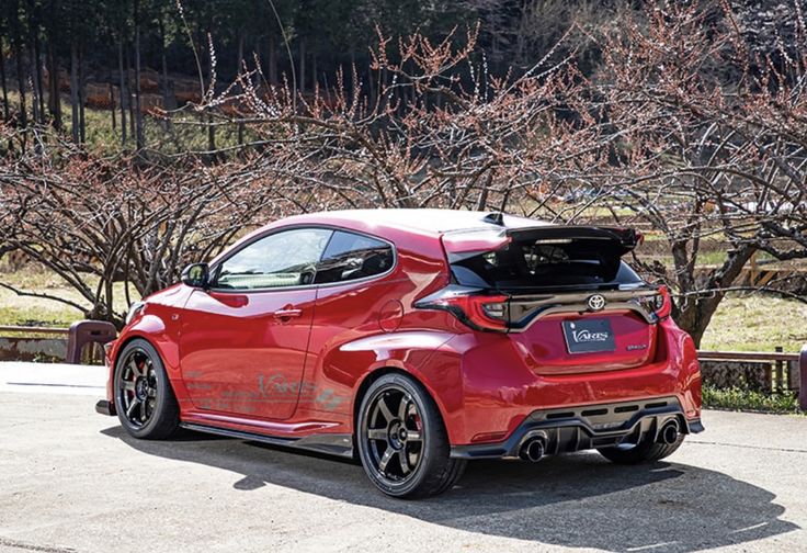 the rear end of a red sports car parked in front of some trees with its trunk open