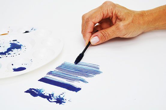 a person is holding a brush and painting with blue ink on a white plate next to the paintbrush