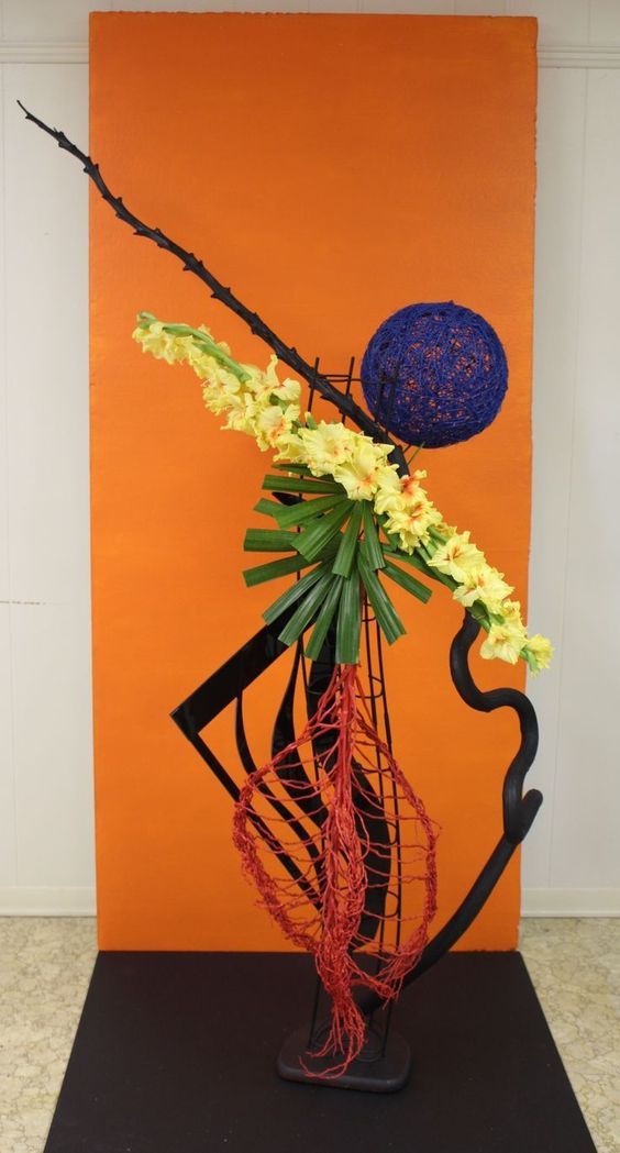 a vase with flowers in it sitting on top of a black stand next to an orange wall