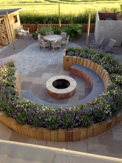 an outdoor fire pit surrounded by plants and flowers