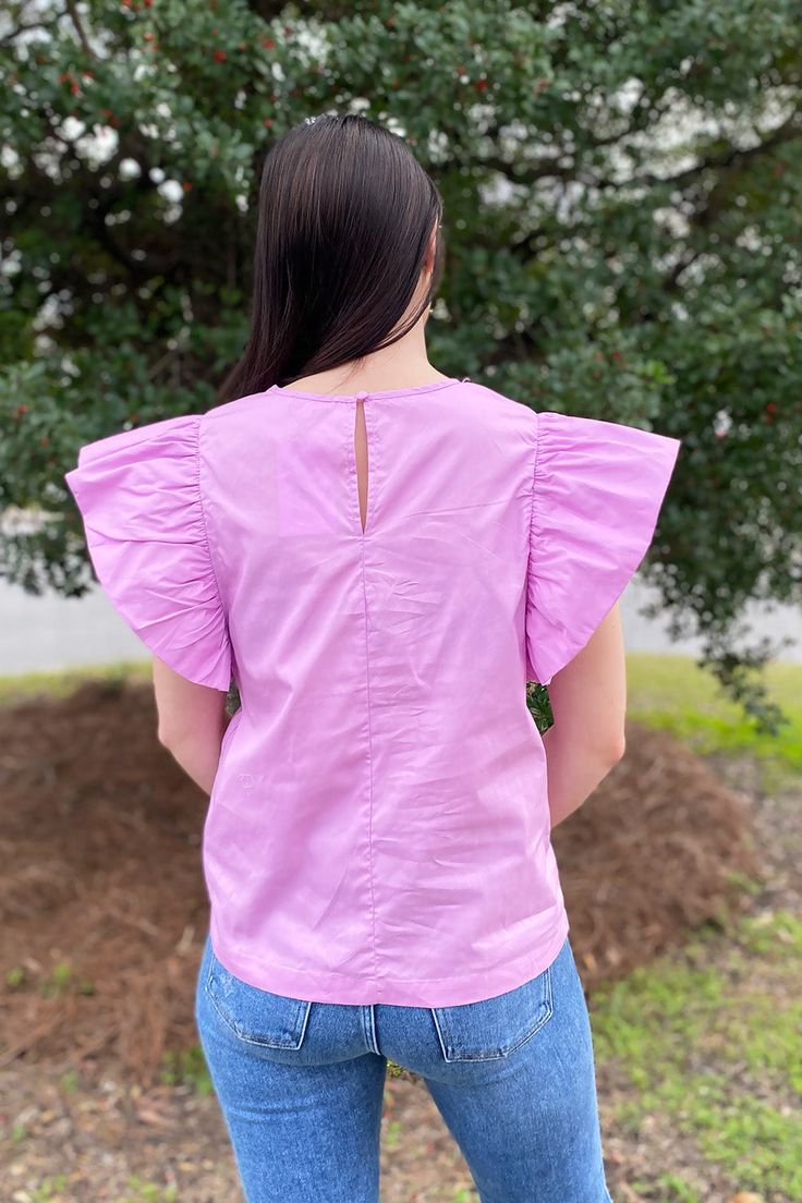 Poplin lavender top with structured ruffle on the shoulders. Buttons at the back of the neck. Model is wearing a size small. Stocked at Arlington Village and Uptown. Purple Flutter Sleeve Tops, Purple Tops With Ruffles And Ruffled Collar, Purple Short Sleeve Top For Brunch, Purple Flutter Sleeve Top For Summer, Feminine Purple Cotton Blouse, Purple Cotton Blouse With Ruffles, Spring Purple Ruffled Blouse, Summer Lavender Blouse With Ruffles, Purple Ruffled Blouse For Spring