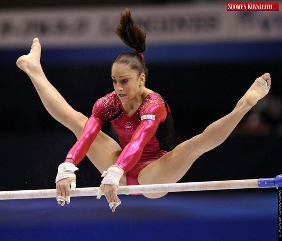 a woman is performing on the beam in an indoor gymnastics match, with one leg bent forward