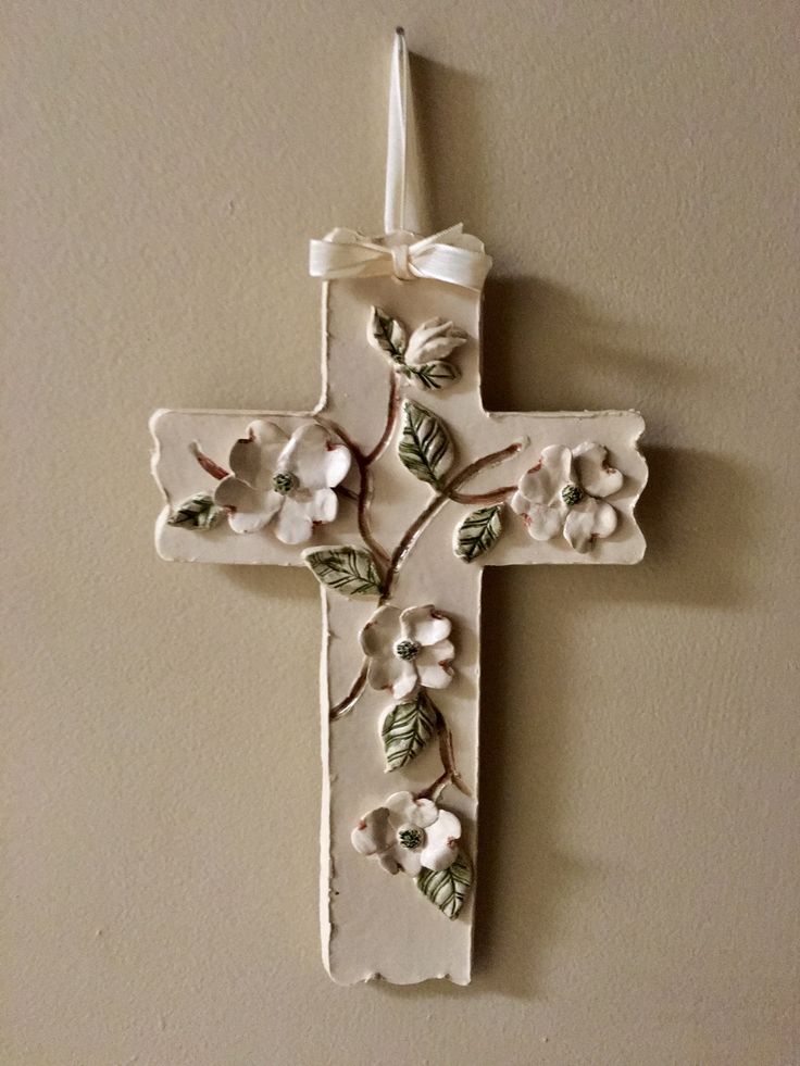 a white cross with flowers on it hanging from the side of a wall in a room