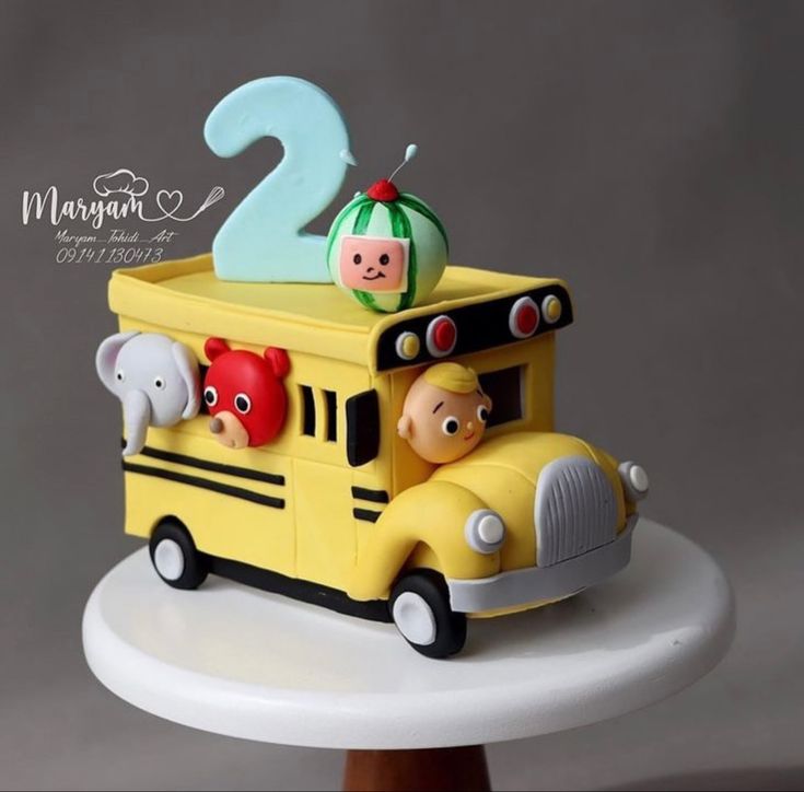 a yellow school bus cake with animals on the front and number two in the back