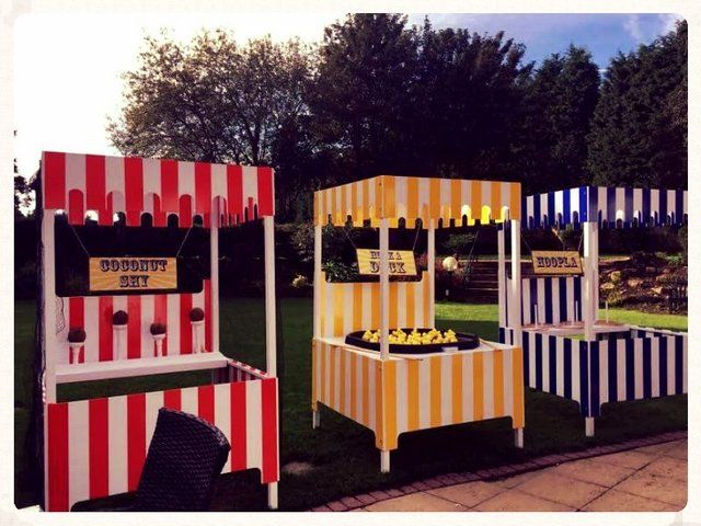 three carnival booths with signs on them sitting in the grass