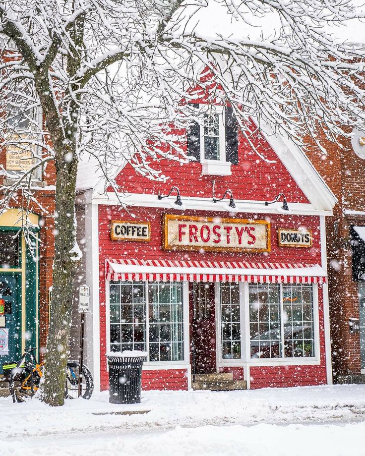 a red and white striped store with snow falling on it's roof, next to a tree