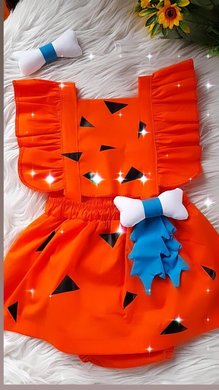 an orange dress with black and blue bows on the front is laying on white fur