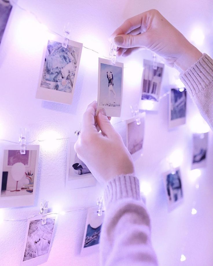 a person holding a card in front of a wall covered with pictures and string lights