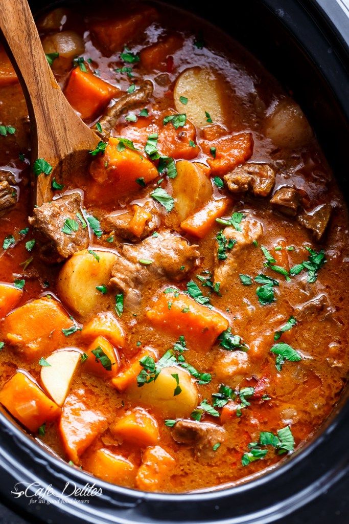 a crock pot filled with beef stew and potatoes, garnished with parsley