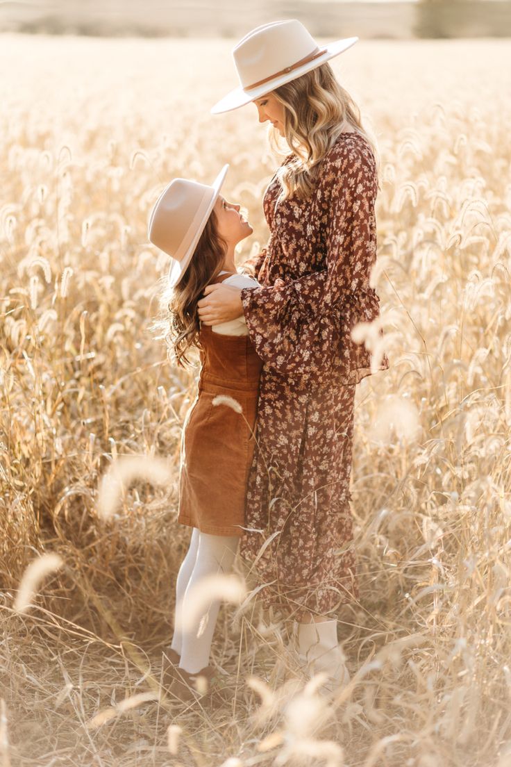 two women standing in the middle of a field with tall grass and one woman wearing a hat