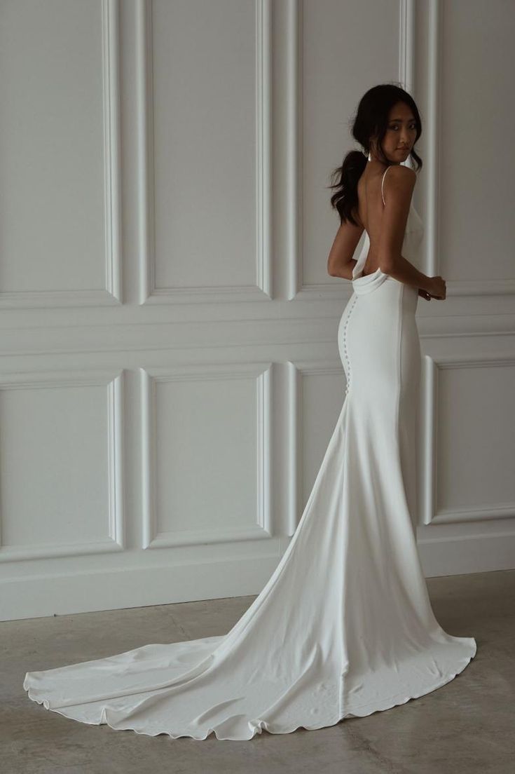 a woman in a white wedding dress posing for the camera with her back to the camera