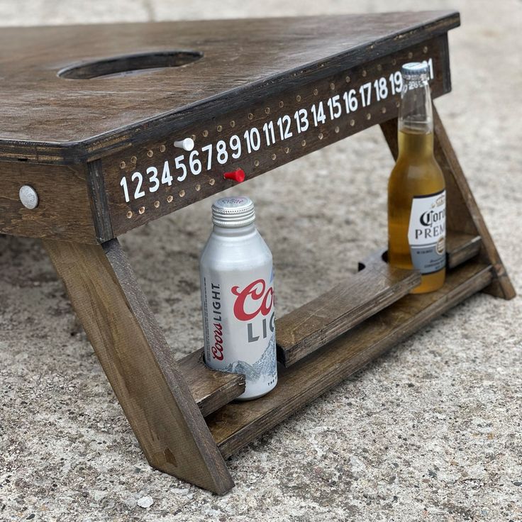 two beer cans sitting on top of a wooden bench with numbers and letters painted on it