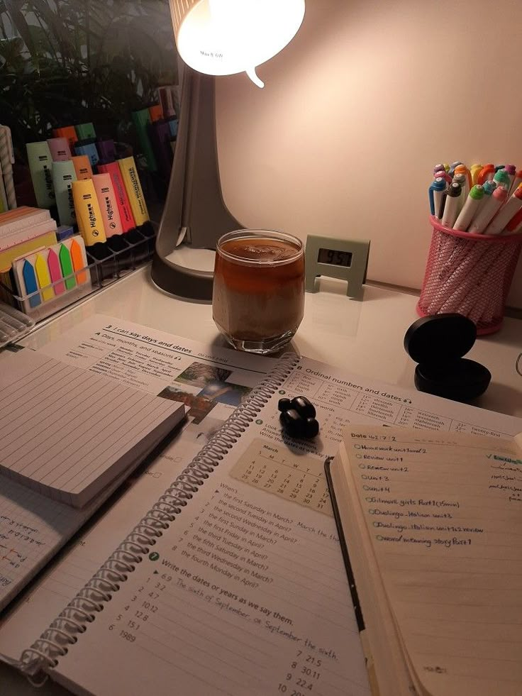 a cup of coffee sitting on top of a desk next to notebooks and pens